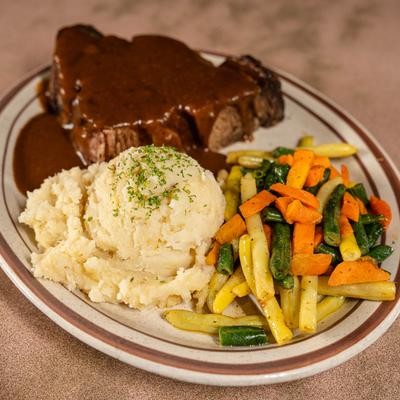 Pot roast covered in gravy, with mashed potatoes and vegetables.