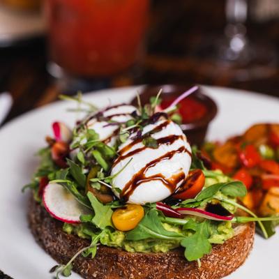Avocado toast topped with poached eggs, fresh arugula, cherry tomatoes, and balsamic drizzle.