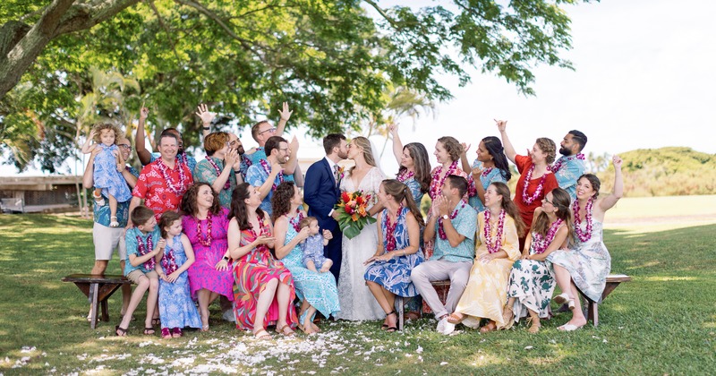 A joyful group of celebrants  gathered outdoors with a wedding couple in the middle