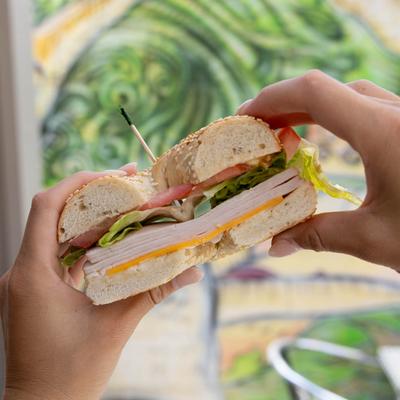 Ham bagel sandwich in hands.