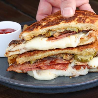 Hand holding a sandwich loaded with melted cheese, bacon and shredded meat.