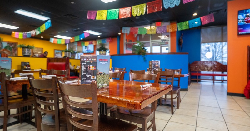 Interior of a colorful restaurant with wooden tables and chairs, vibrant papel picado banners