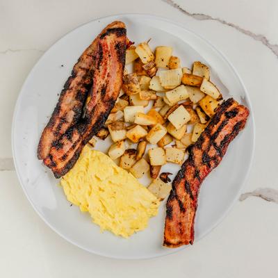Breakfast plate featuring scrambled eggs, bacon and potatoes.