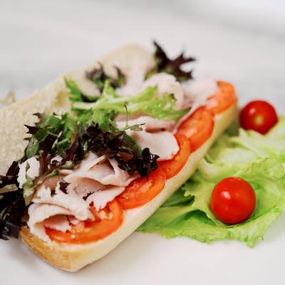 A turkey and vegetable sandwich on a white plate, garnished with lettuce and cherry tomatoes.