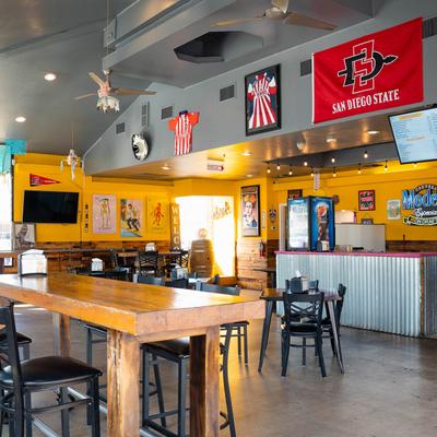 Interior with yellow walls, wooden tables, sports jerseys, and TVs.