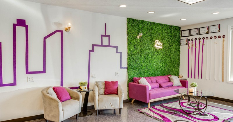 Seating area, with pink sofa, grey armchairs, cushions, and an artificial grass wall