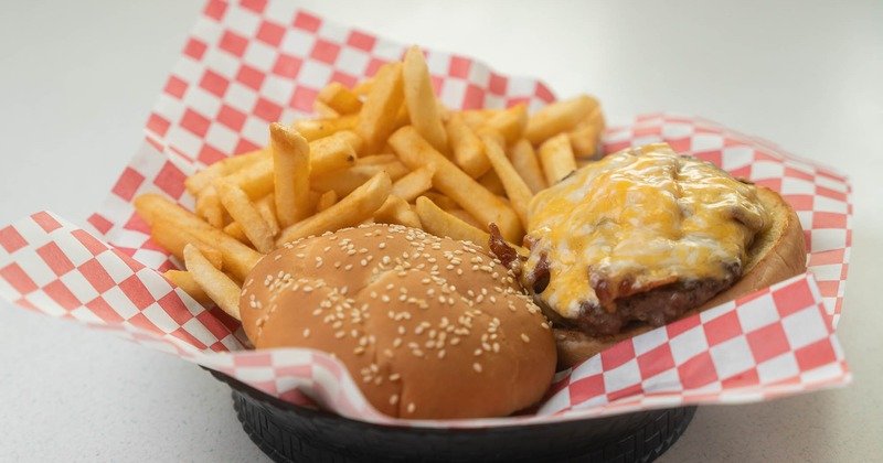 A basket with golden fries and American burger on red checkered paper