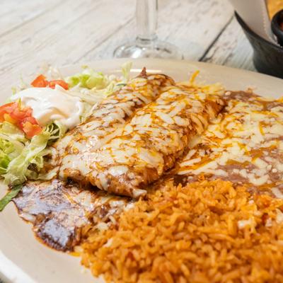 Enchiladas topped with mole sauce and melted cheese, served with rice and beans.