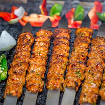 Skewers of grilled minced meat cook with sliced peppers and onions.