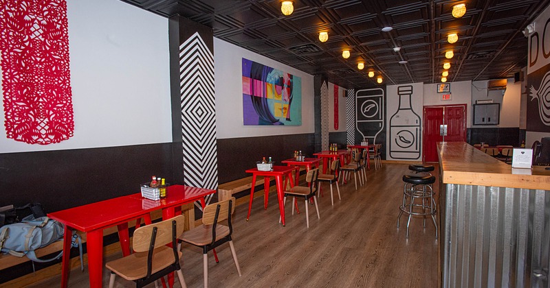 Interior of a modern dining space with red tables, wooden chairs, abstract artwork