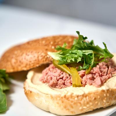 Bagel sandwich with ham, hummus spread, lettuce, and pickles.