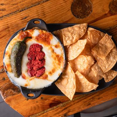 Melted cheese dip served with tortilla chips, garnished with chorizo and a green chili.