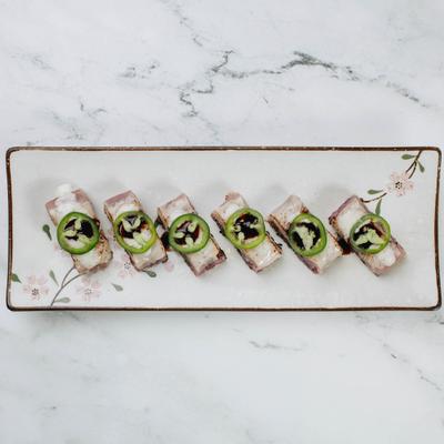 Sushi roll topped with jalapeno slices and sauce.