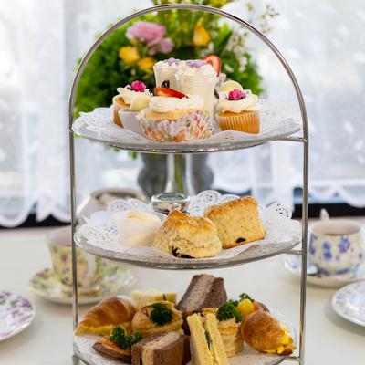 Three-tiered dessert stand with cupcakes, scones, and assorted sandwiches.