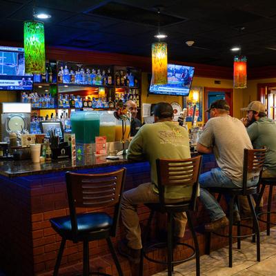 People at the bar with TVs, pendant lights, and liquor bottles.
