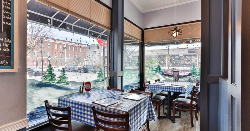 Interior with checkered tablecloths and large windows showcasing winter-themed paintings