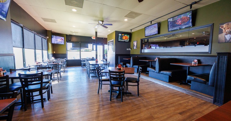 A modern restaurant interior with wooden tables, black chairs, booths, and TVs on the walls