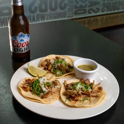 Pulled pork street tacos served with green sauce, accompanied with a bottle of beer.