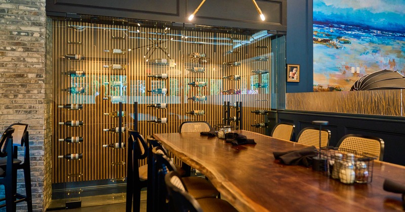 Interior - wooden table, black chairs, a glass wine cabinet with bottles; artwork on the wall