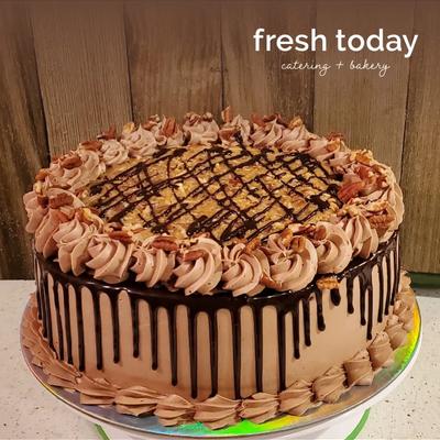 Chocolate-drizzled cake with swirled frosting and nut garnish on a decorative plate.
