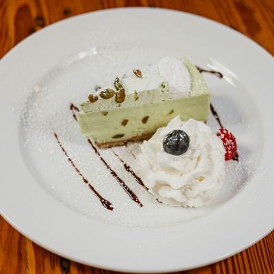 A slice of pistachio cheesecake served with whipped cream on a white plate