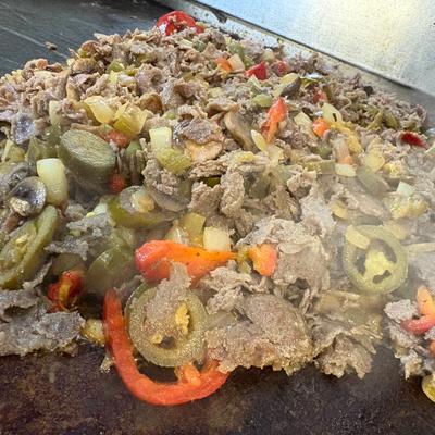 Meat and vegetables cooking on a griddle.