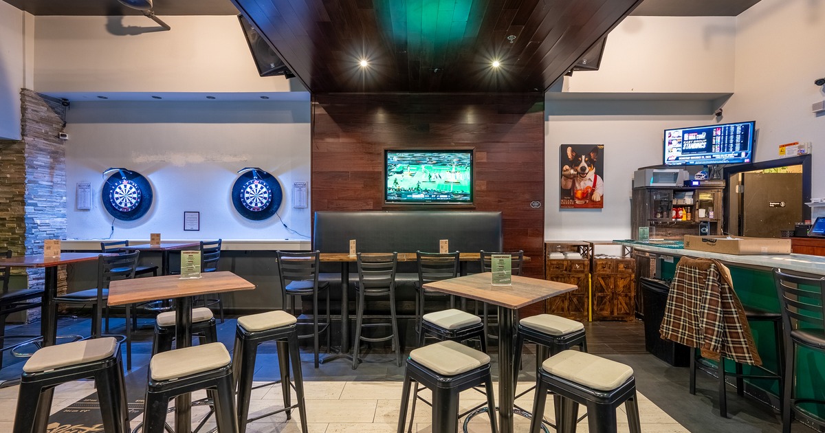 Sports bar interior with tall bar stools and high tables and two electronic dartboards on the wall