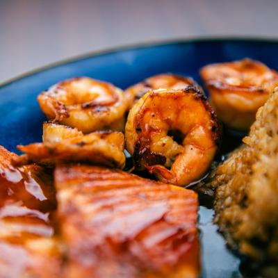 Grilled shrimp with glazed salmon and rice on a blue plate.