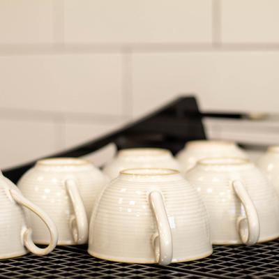 White ceramic coffee cups rest upside down on a black mesh warming tray.