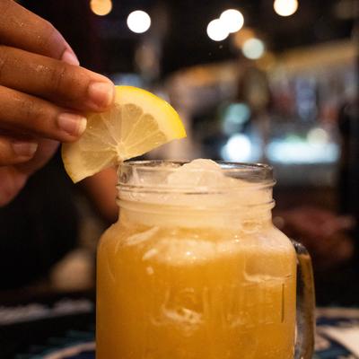 A person places a lemon wedge on the rim of a mason jar with peach drink.