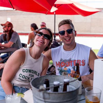 Two friends posing together at an outdoor table under red umbrellas.