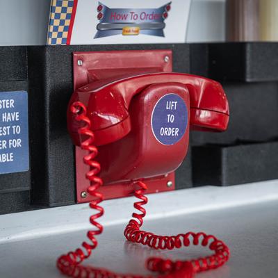Red wall-mounted rotary phone labeled Lit to Order.