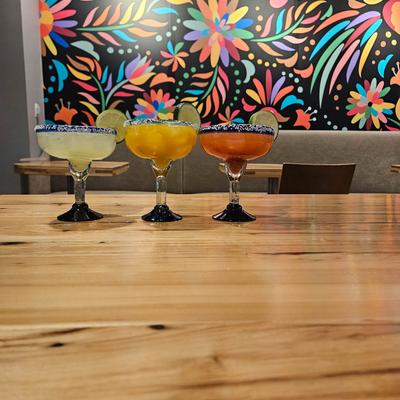 Three colorful margaritas on a wooden table against a wall mural.
