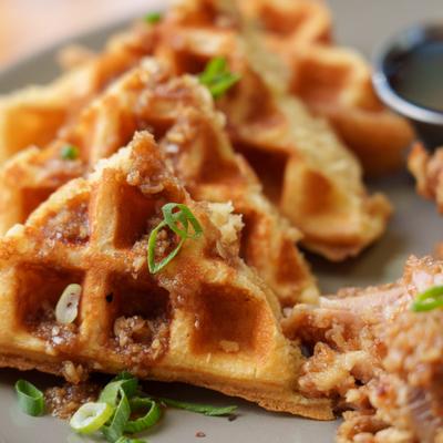 Waffles topped with green onions, with fried chicken and syrup on the side.