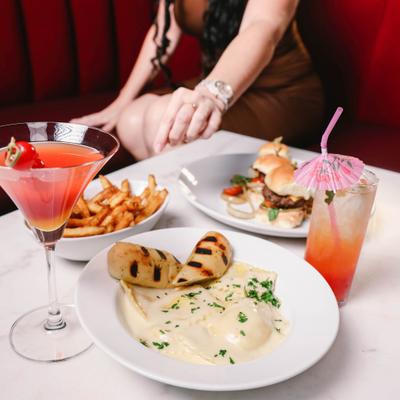 Pasta dish served alongside plate of sliders, fries and cocktails.