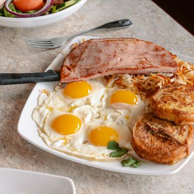 Breakfast platter with fried eggs, slice of grilled ham, hash browns and French toast.