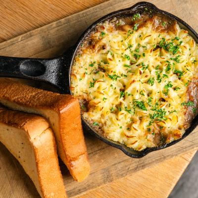Skillet with Shepherds pie served on a wooden boeard with toated bread.
