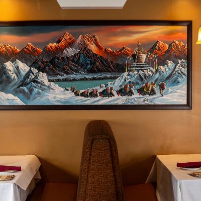 A painting depicts a snowy mountain scene with a caravan of yaks, it hangs above a booth.