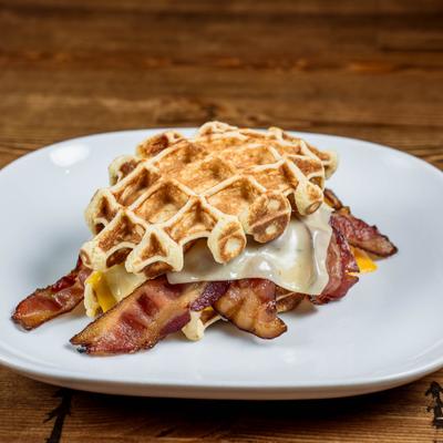 Breakfast waffle sandwich featuring crispy bacon, egg and melted cheese.
