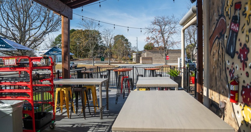 Outdoor patio with tables, stools, string lights, umbrellas and a mural.