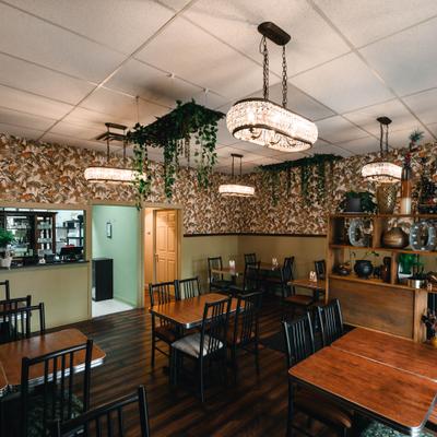 Interior of the restaurant with patterned wallpaper, wood tables, chairs, and decorative shelving.