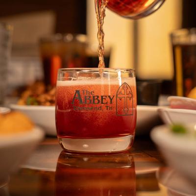Beer being poured into The Abbey glass on a table filled with food, close up.