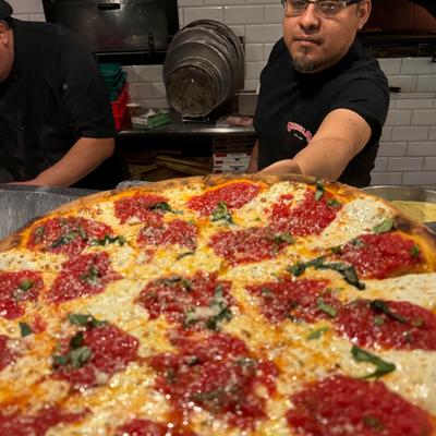 A staff member holding a whole pizza.