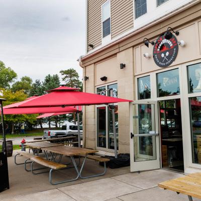 Storefront with entrance, signage, wooden picnic table and red umbrellas.