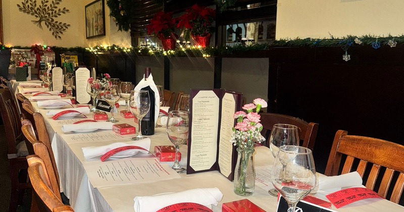 A festive interior with a long dining table with place settings, glasses, wine and menus