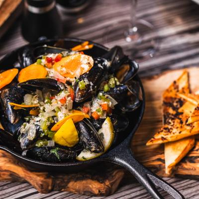 Mussels with vegetables in a black skillet with toasted bread on the side.