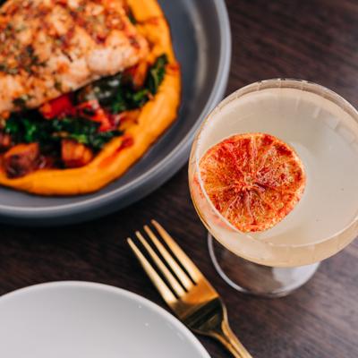 Salmon with Carrot Tahini Puree, Sweet Potatoes, Grilled Peppers, Kale and Smoked Paprika vinaigrette, along with a cocktail..