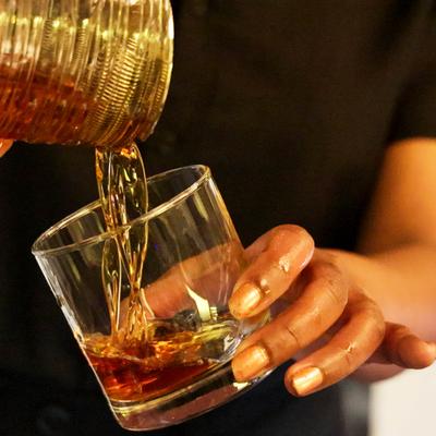 Whiskey being poured into a clear, heavy-bottomed rock glass.