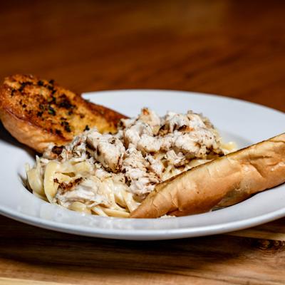 Chicken Alfredo pasta with creamy sauce, served with grilled bread.