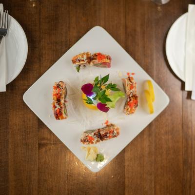 Flaming sushi appetizer presented on a large white plate on a square table.